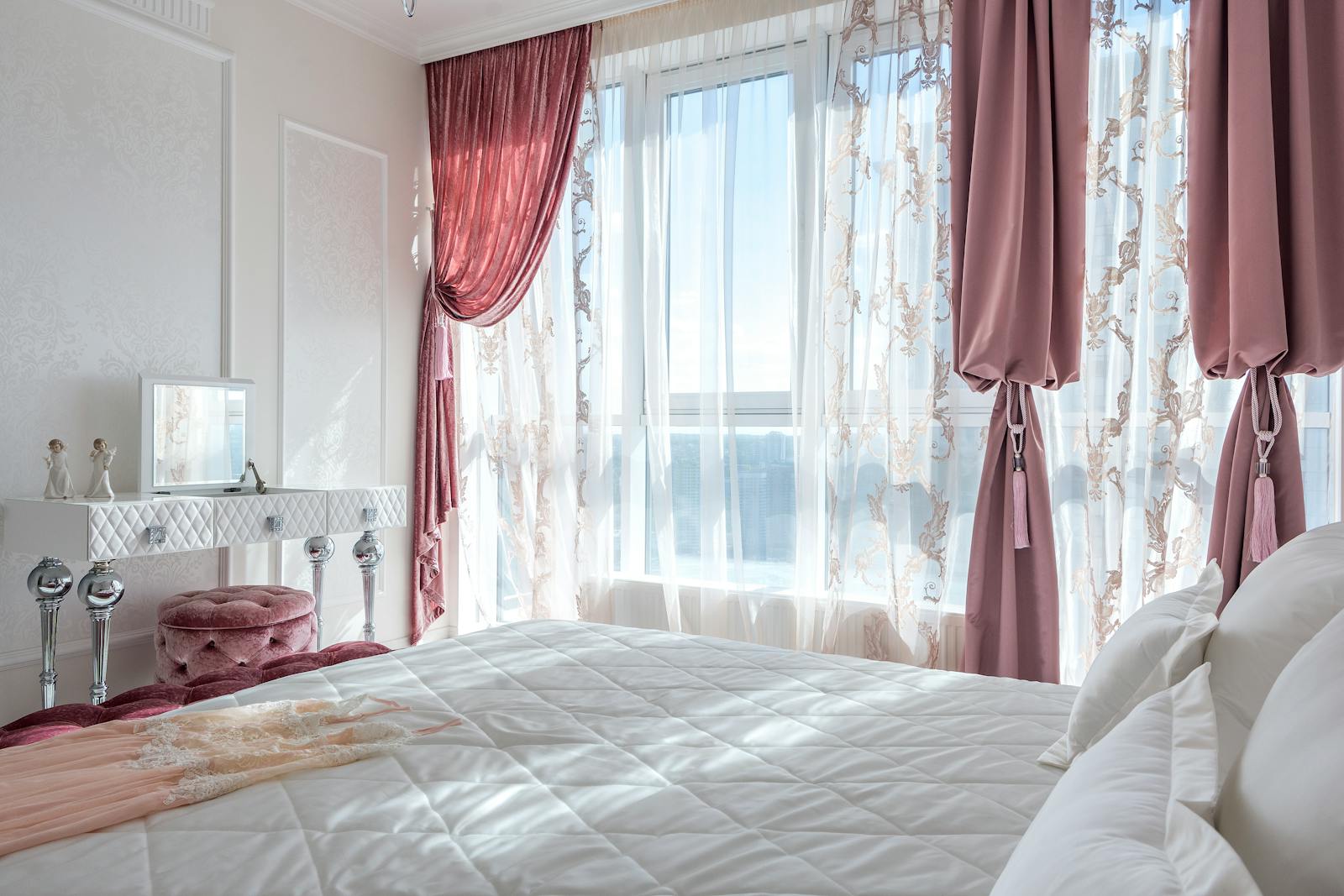 Bright, elegant bedroom with chic decor, featuring pink drapes and a comfortable bed, exuding luxury and style.