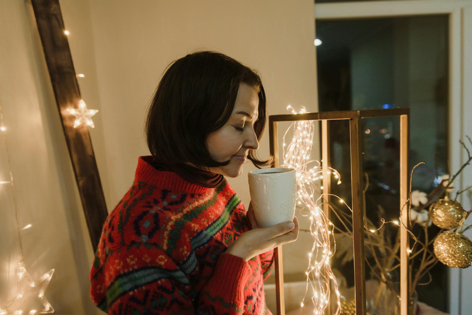 Woman enjoying a warm drink indoors with festive winter decorations
