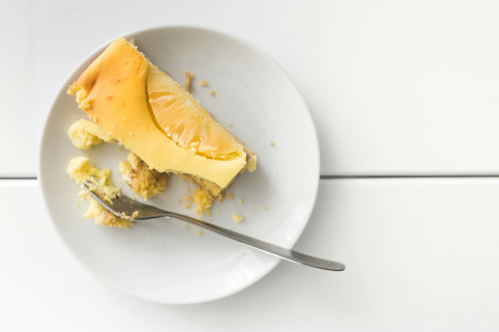 Delicious slice of cheesecake topped with pineapple, served on a white plate.