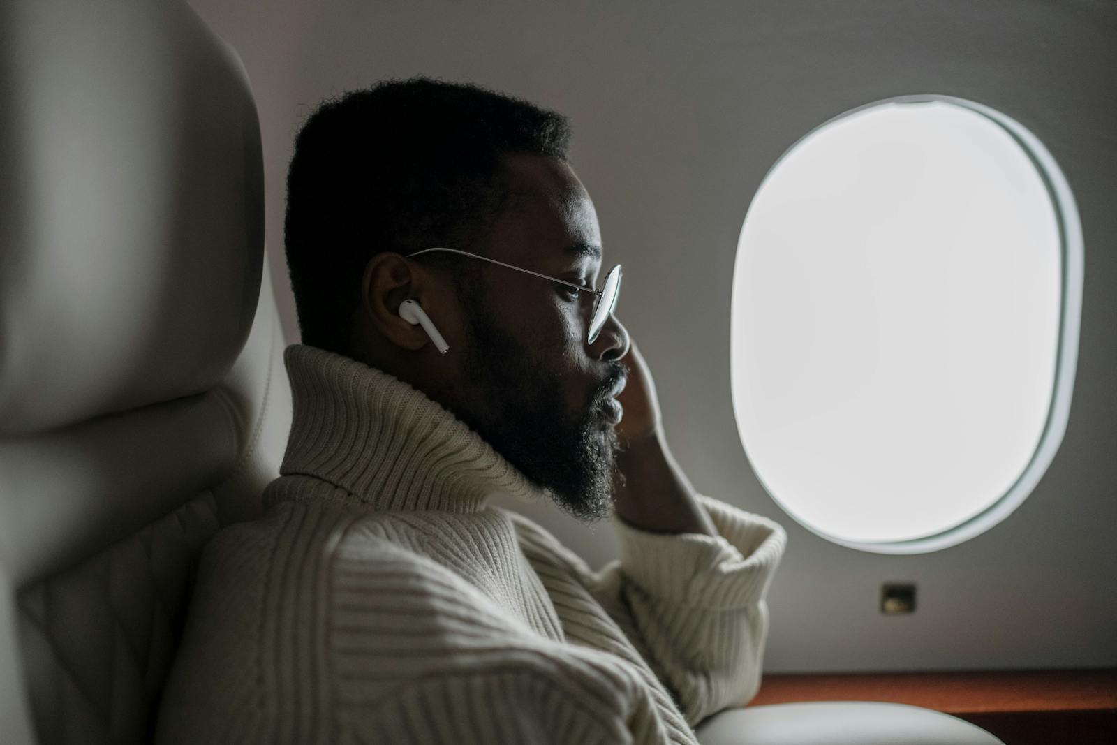 A businessman listening to music on an airplane, sitting by the window in a cozy sweater.