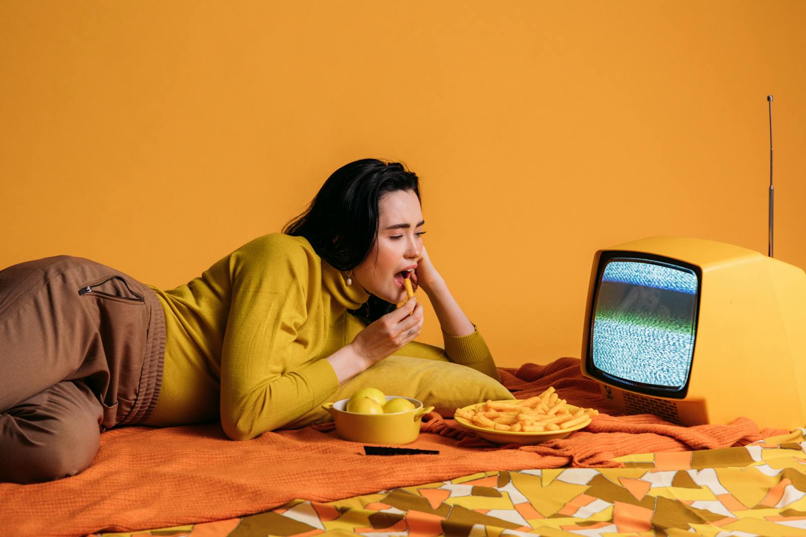 Woman dining on snacks while watching a vintage TV in a retro, colorful setting.
