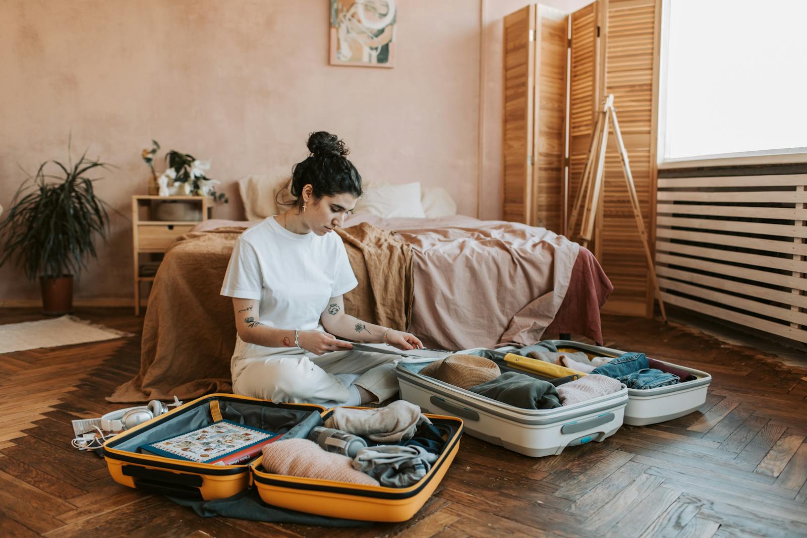 A woman organizes luggage in a stylish bedroom, carrying wanderlust vibes.