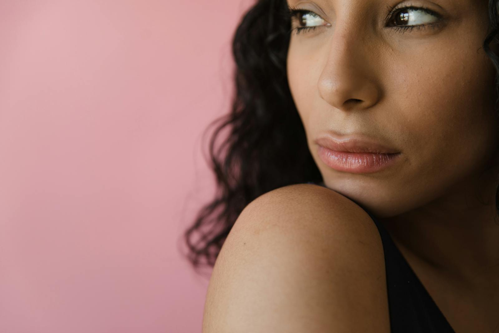 Close-up of a woman looking sideways with a pink background.