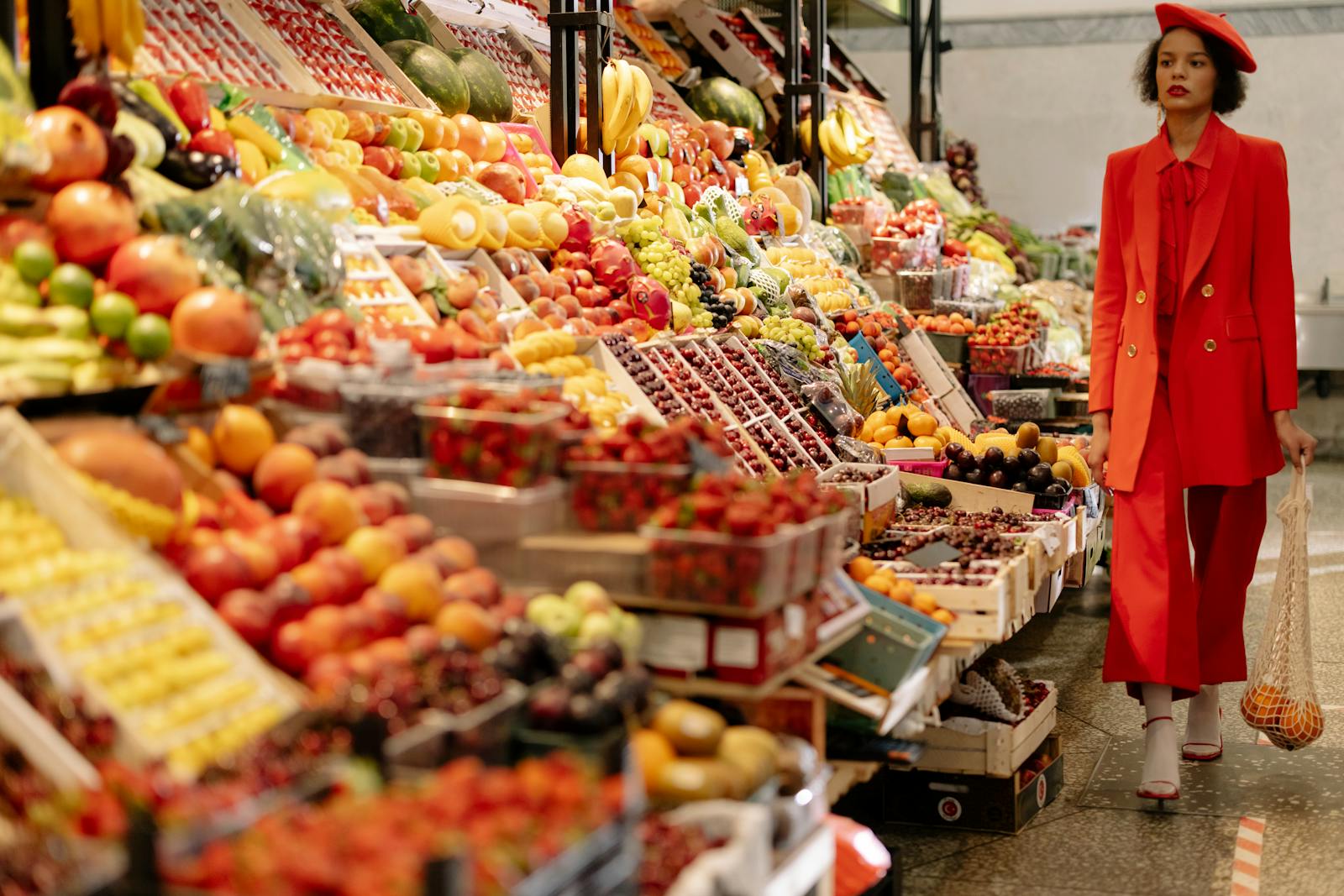 Stylish woman in red outfit shopping for fresh fruits at a bustling market.