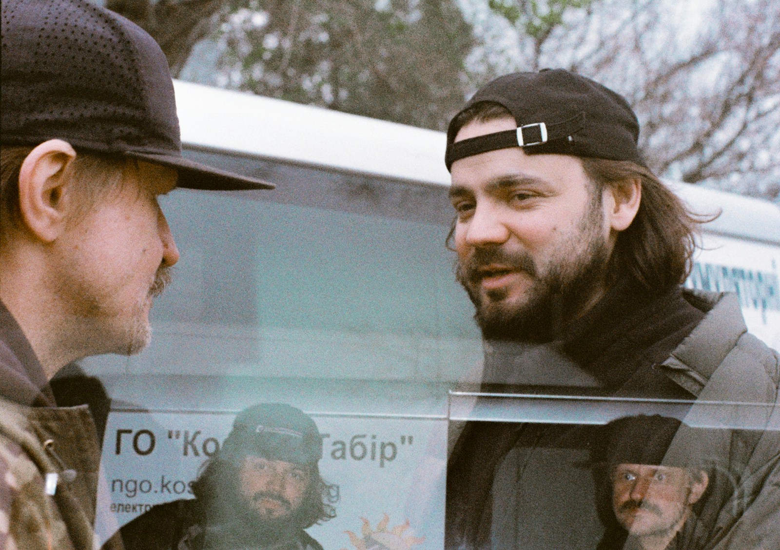Two men talking near a bus with text.