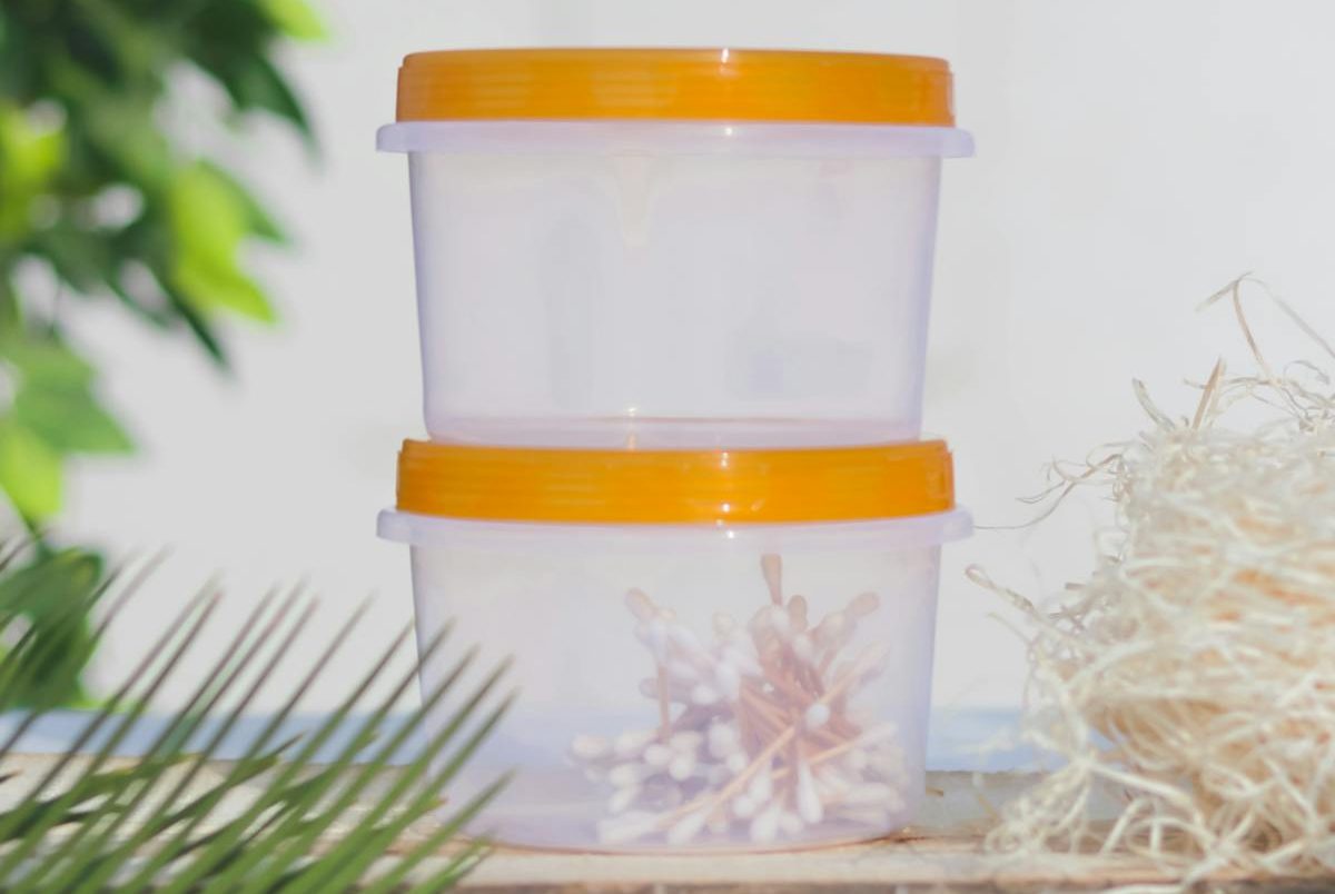 Two stacked plastic containers with cotton buds and orange lids in an outdoor setting.