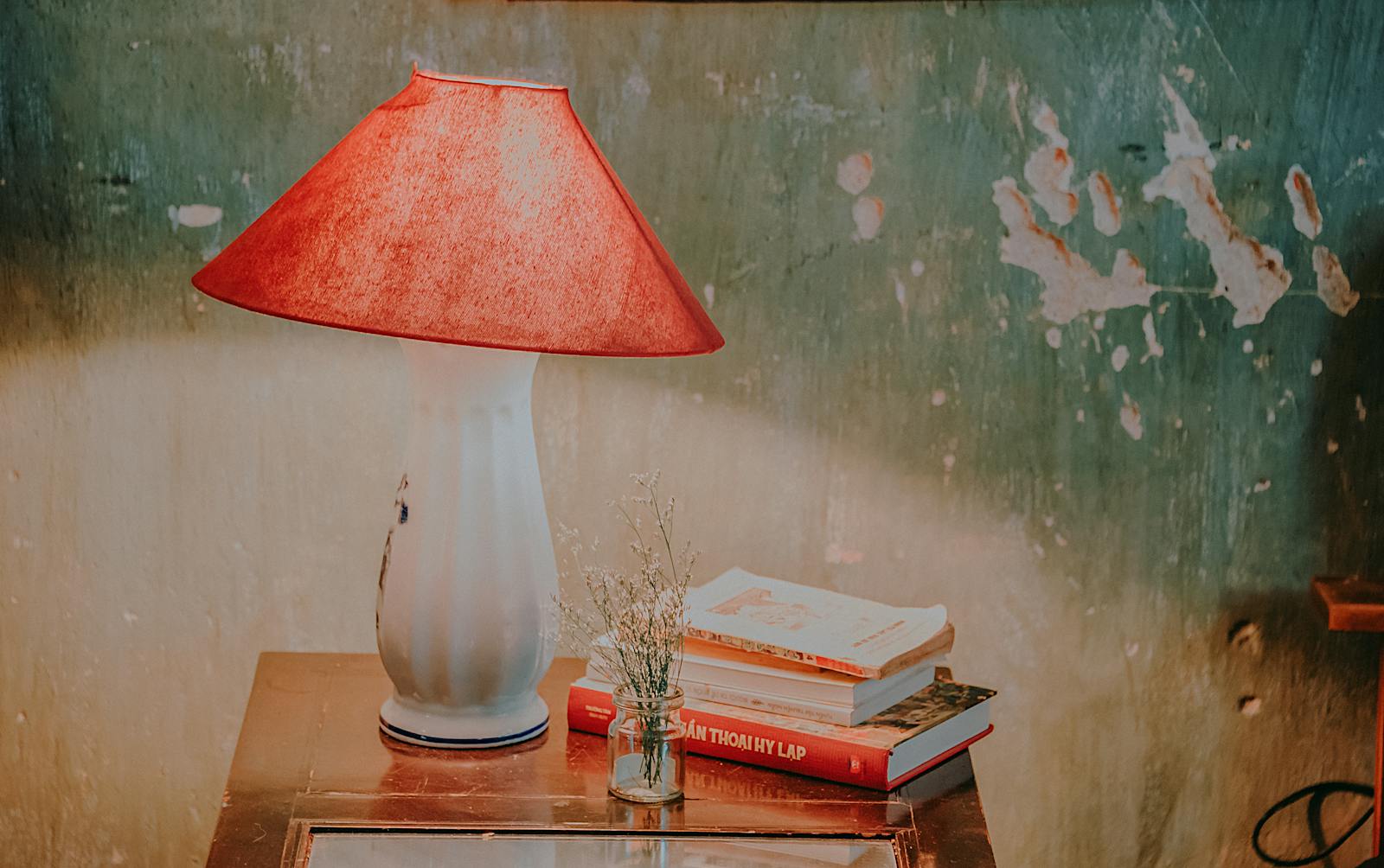 Warm and cozy rustic interior featuring a vintage lamp, books, and a weathered wall.