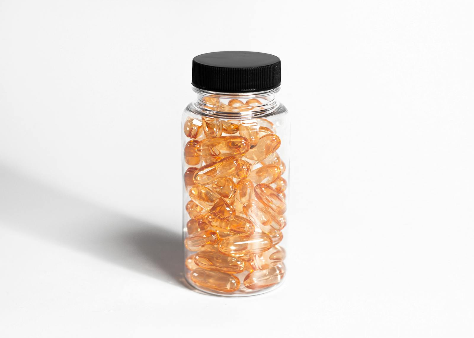 A transparent bottle filled with amber capsules against a white background, showcasing health and nutrition.