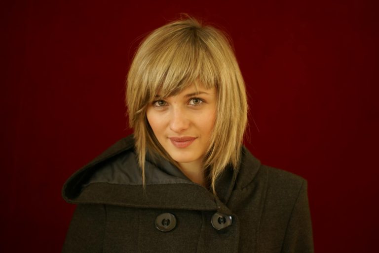 Chic portrait of a woman in a coat with a red backdrop, highlighting her modern style and elegance.