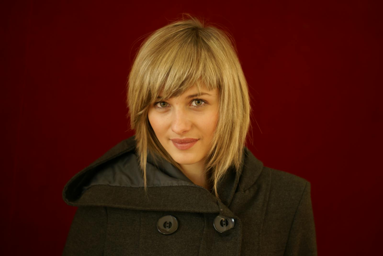 Chic portrait of a woman in a coat with a red backdrop, highlighting her modern style and elegance.