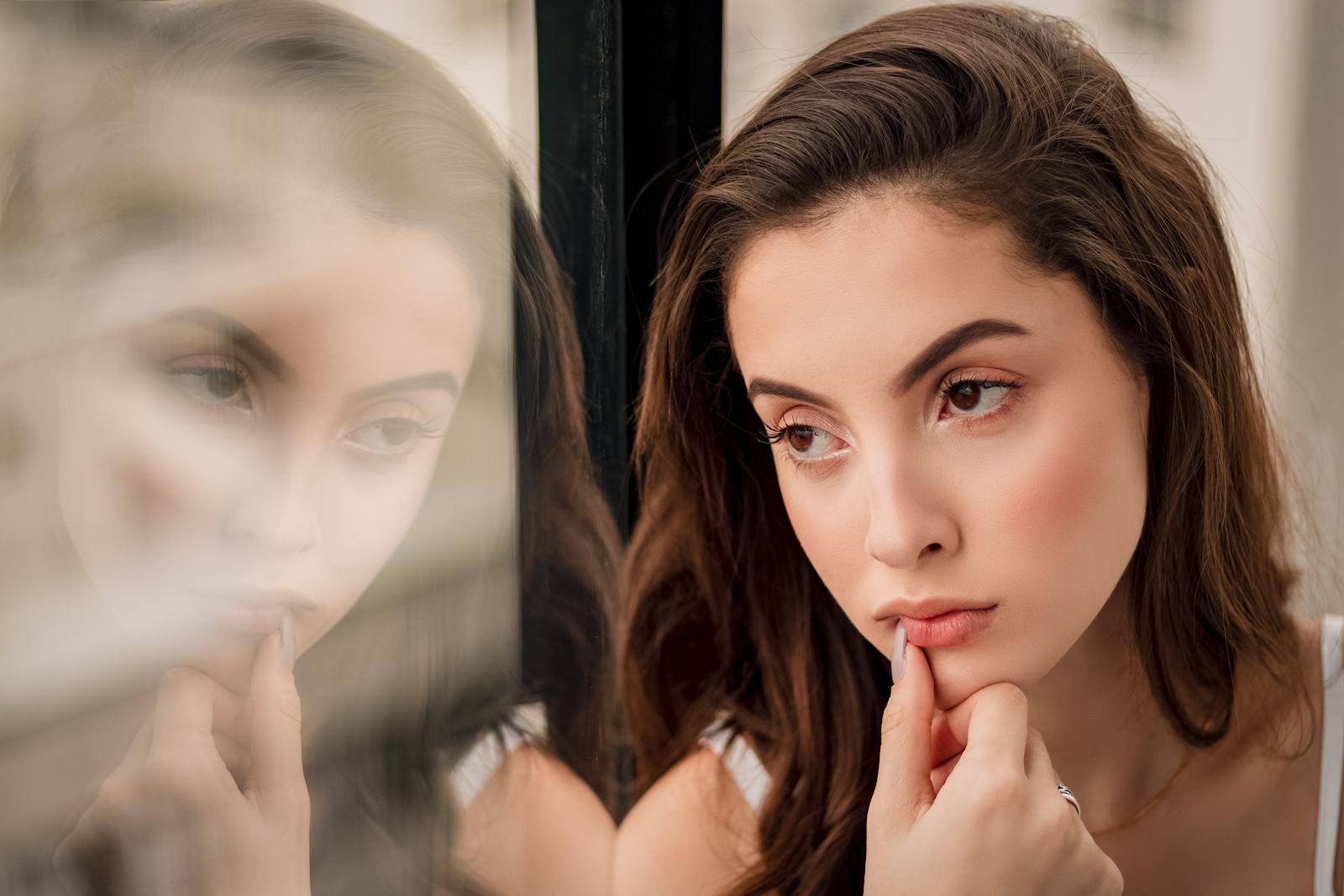 A pensive woman looks out a window, her reflection creating a thoughtful portrait.