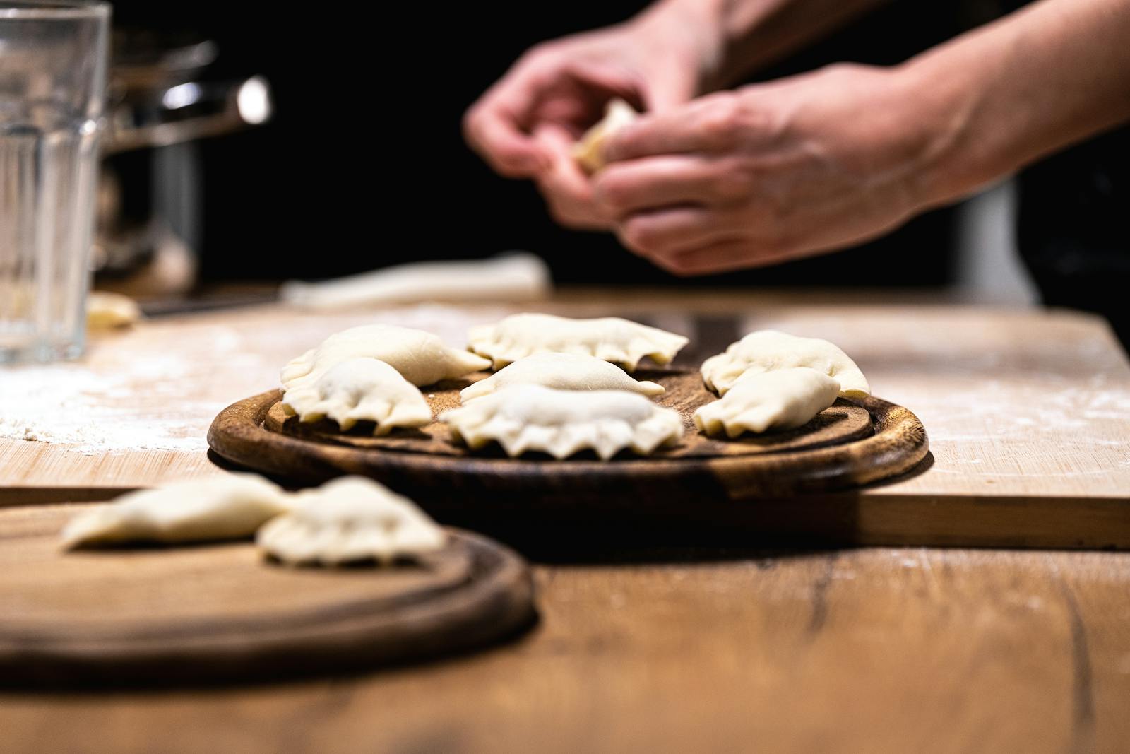 Hands preparing fresh homemade dumplings on a wooden board in a cozy kitchen.