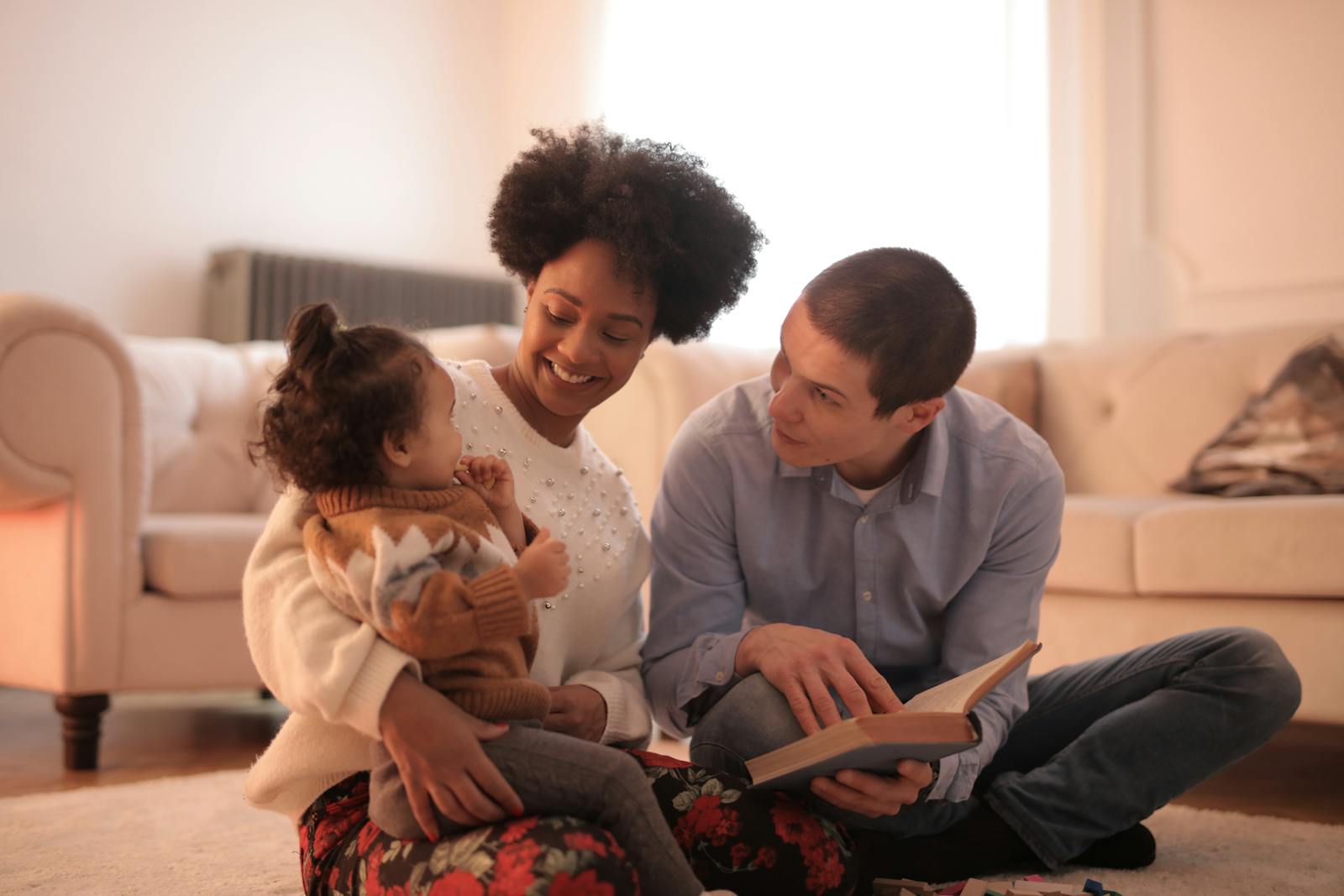 Loving parents reading with cheerful toddler in cozy living room, embracing family time.