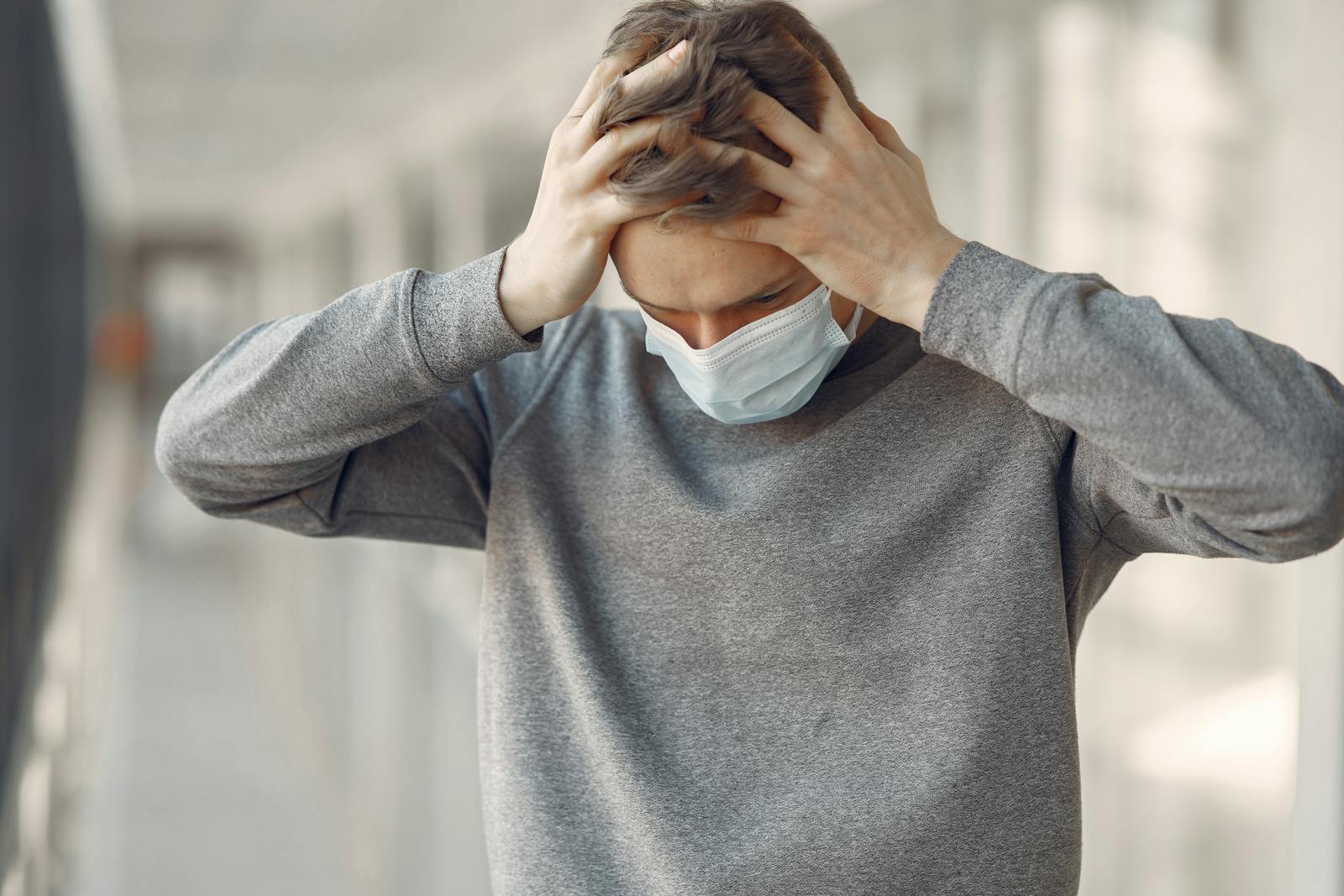 Adult male wearing a face mask, appearing stressed and worried while standing indoors.
