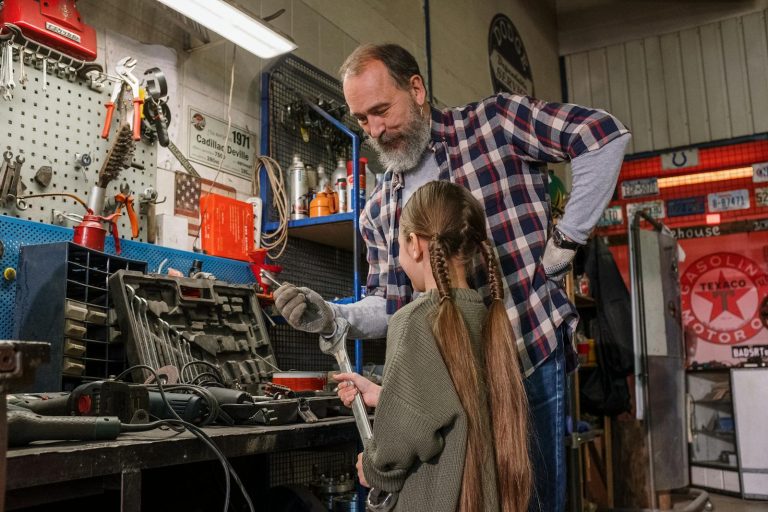 A father and daughter bonding over tools in an auto repair workshop, in a warm family moment.