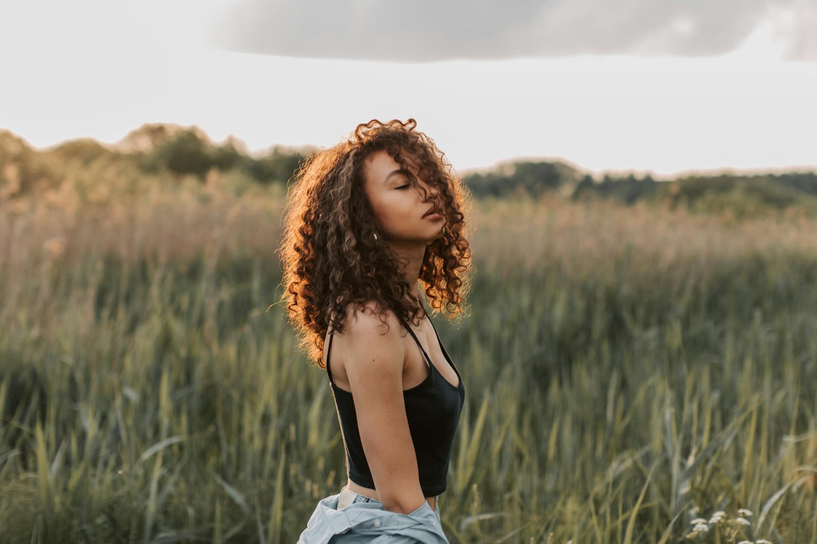 Beautiful woman with curly hair enjoying a summer day in a green field.