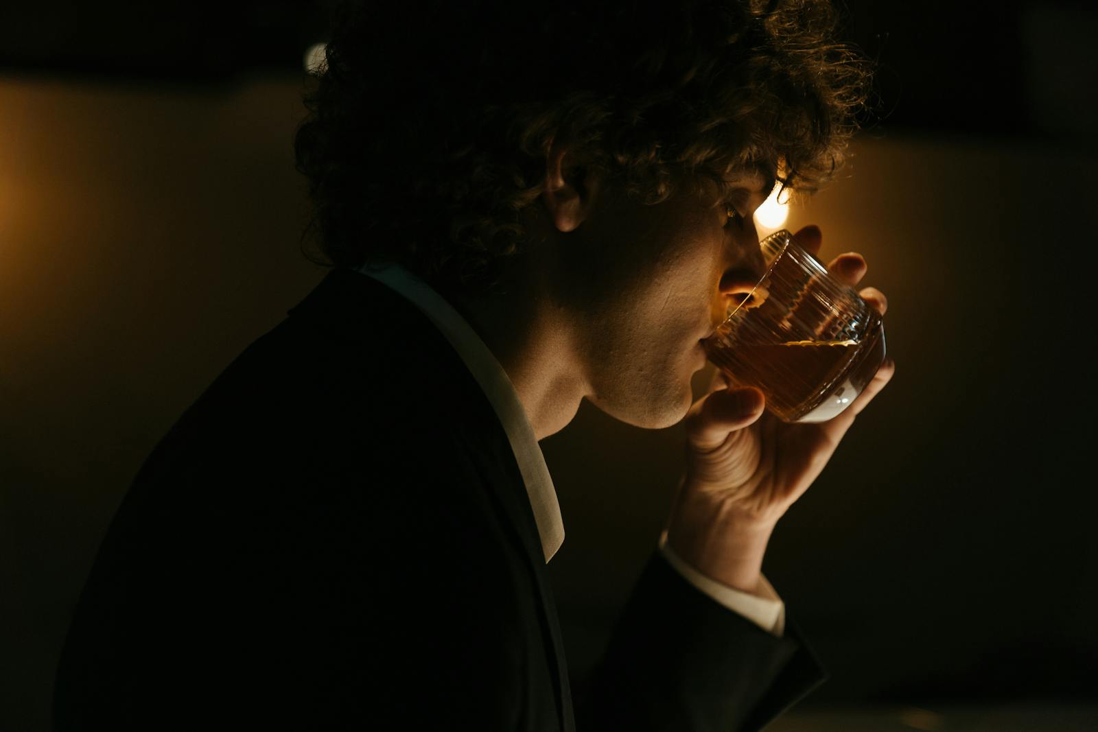 A stylish young man in a suit enjoying a drink at a dimly lit bar.
