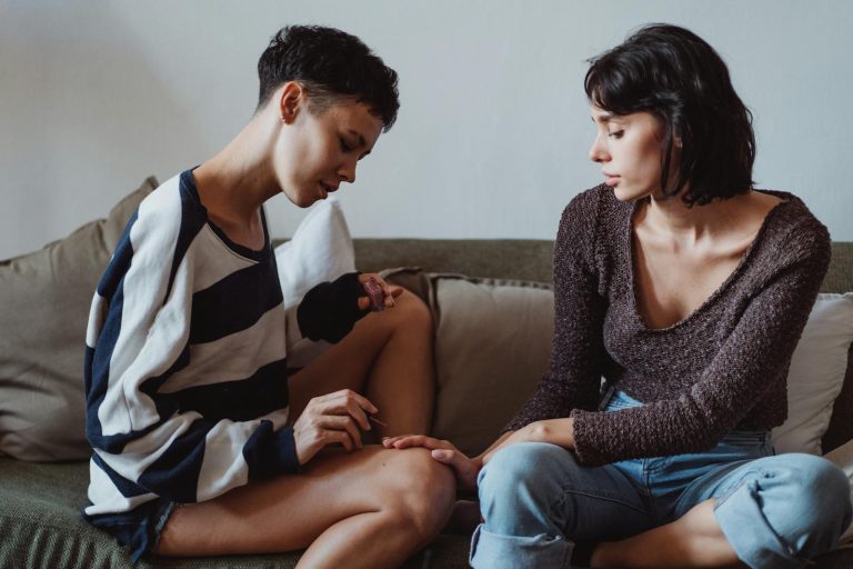 Two women having an intimate conversation seated on a cozy couch indoors.