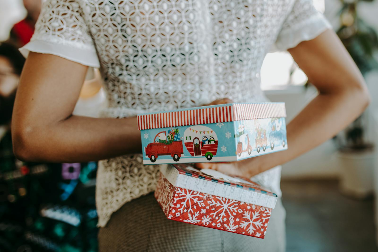 Person hiding colorful Christmas gift boxes behind their back, creating a playful festive surprise.