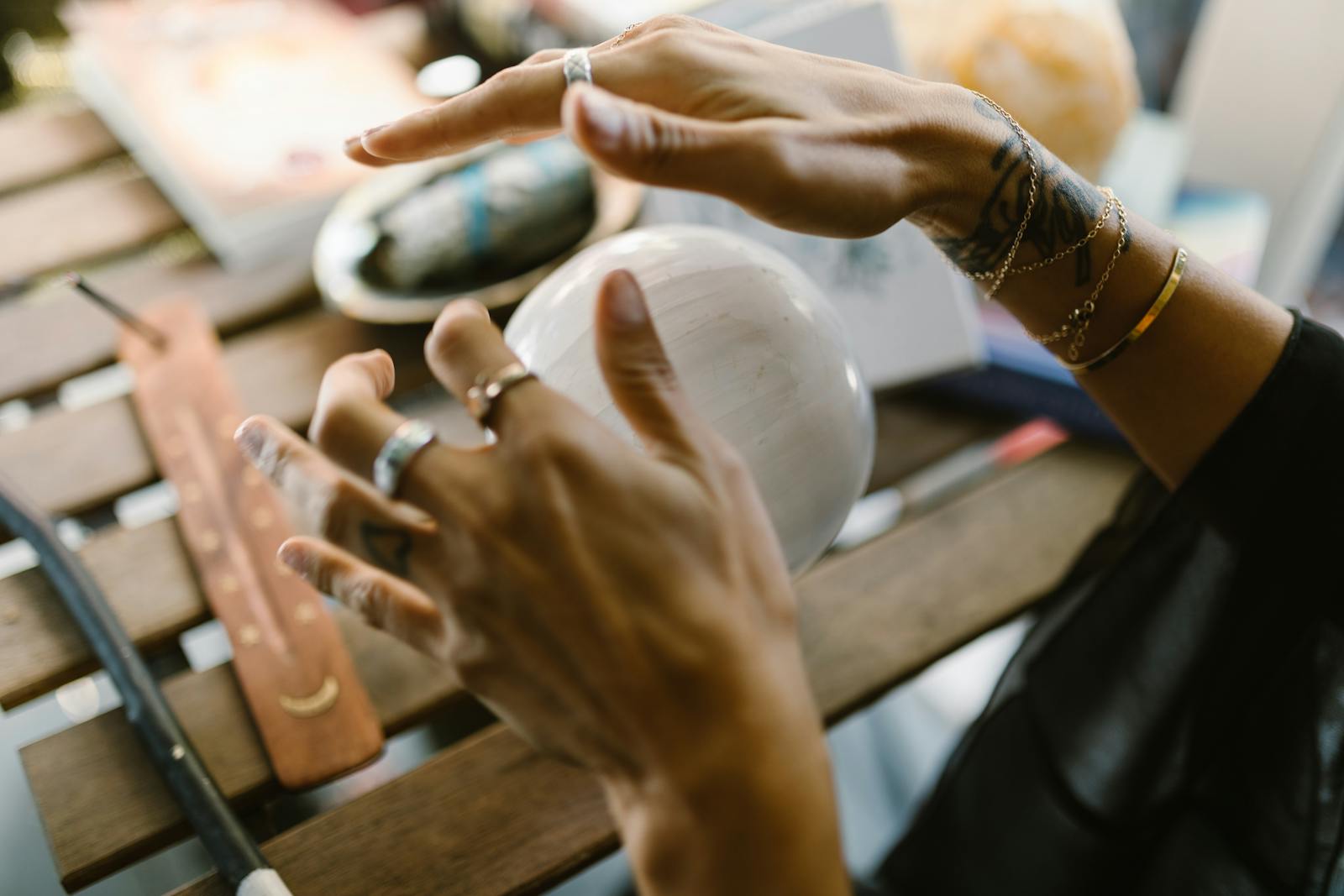 A close-up of hands with jewelry interacting with a mystical crystal ball on a wooden table.