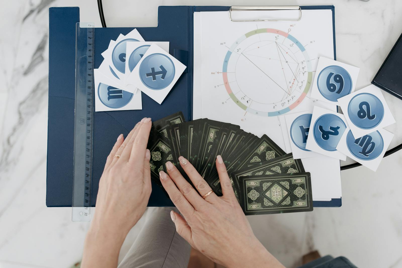 Hands arranging tarot cards with astrology symbols and natal chart on a table.