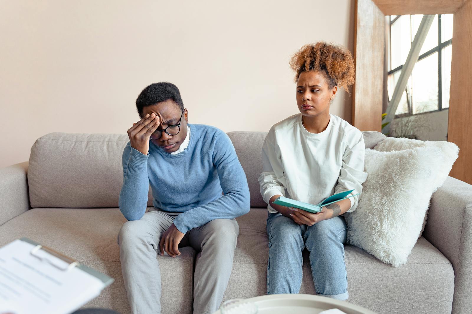 Two people sitting on a sofa indoors, engaged in a serious discussion during a therapy session.