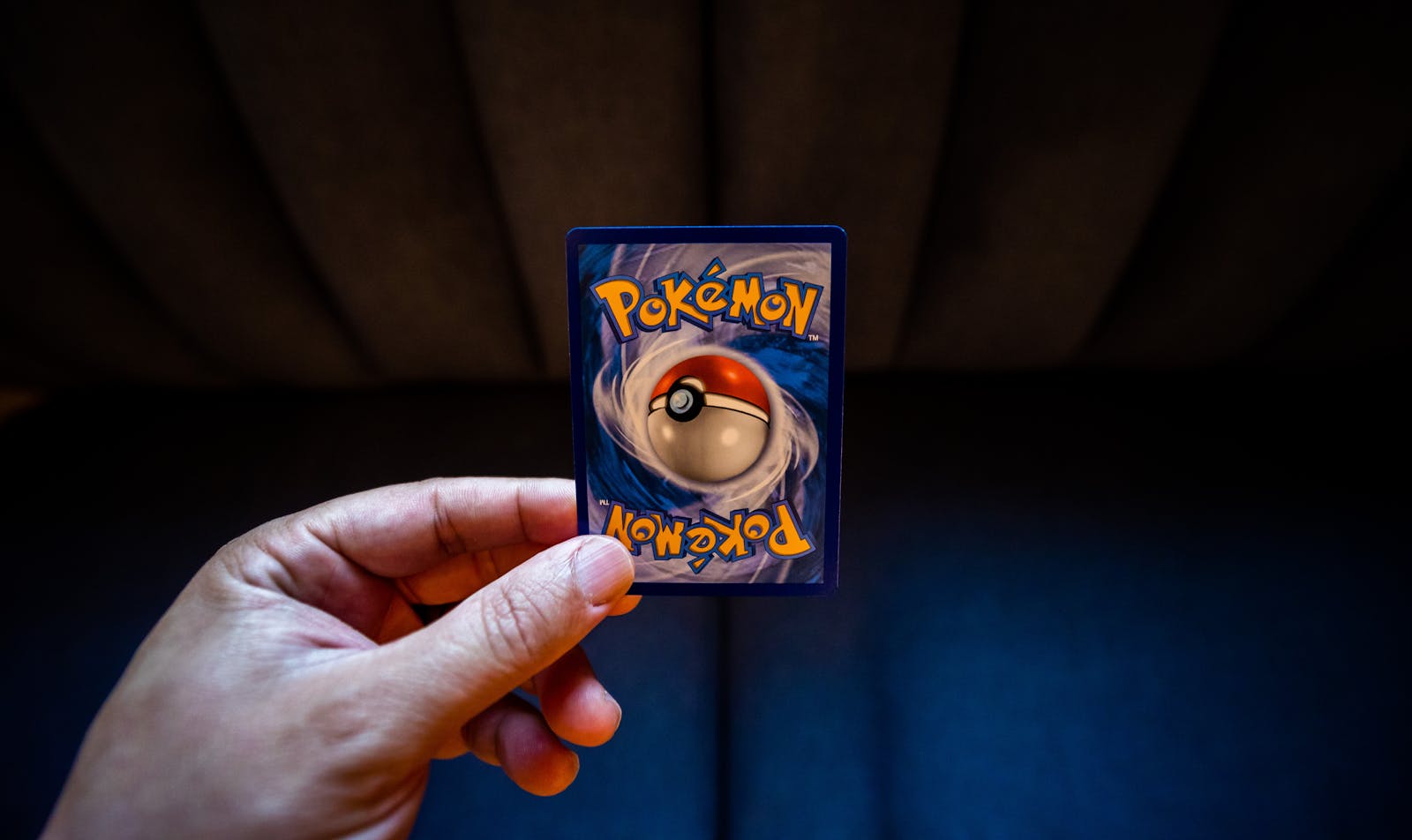 A hand holds a Pokémon trading card with a dark background, emphasizing gaming culture.