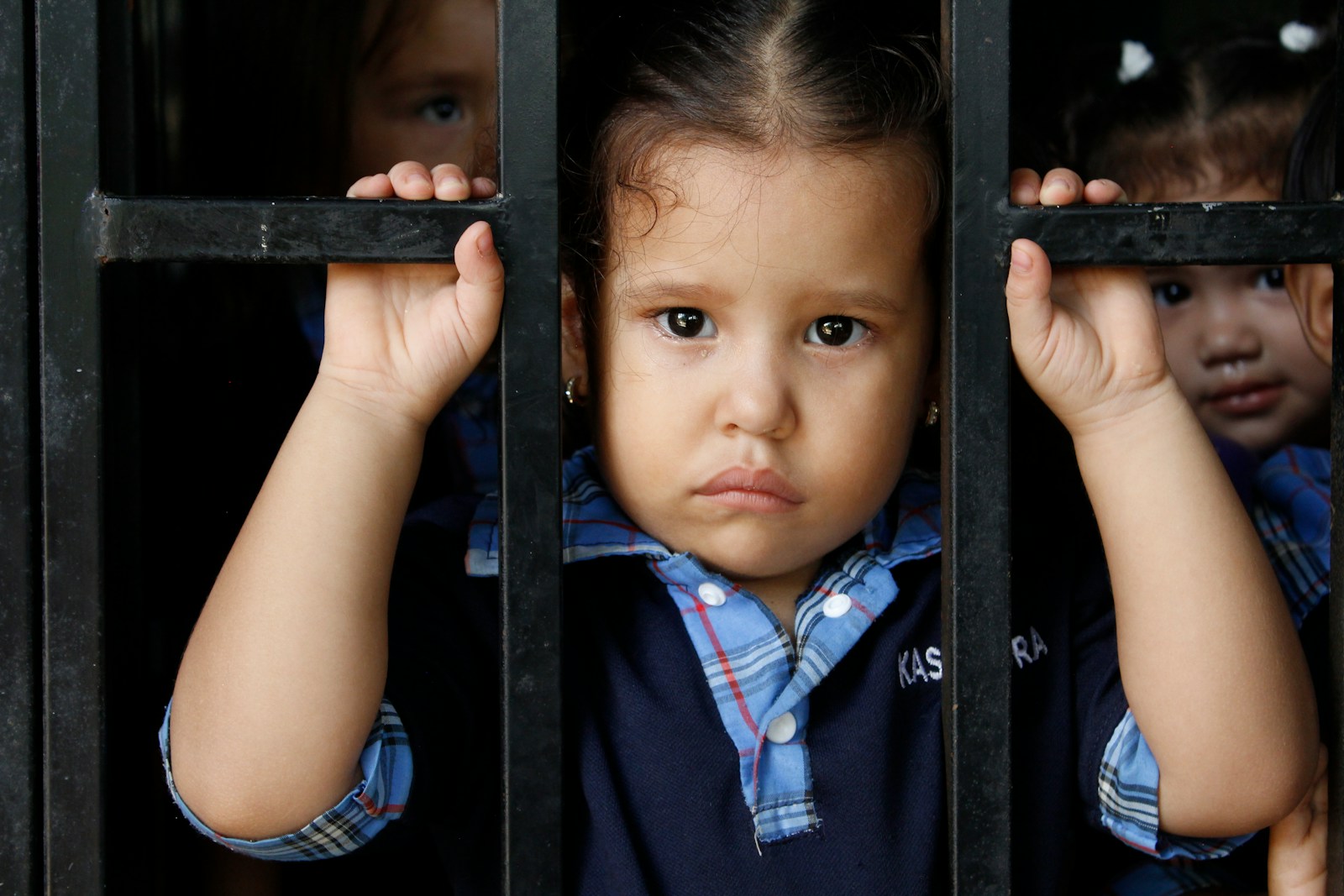 Three young children behind a metal grate
