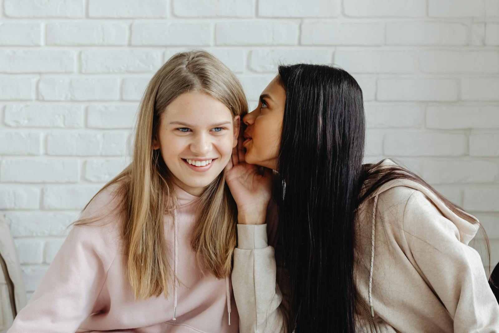 Two teenage girls whispering indoors, sharing secrets and friendship.