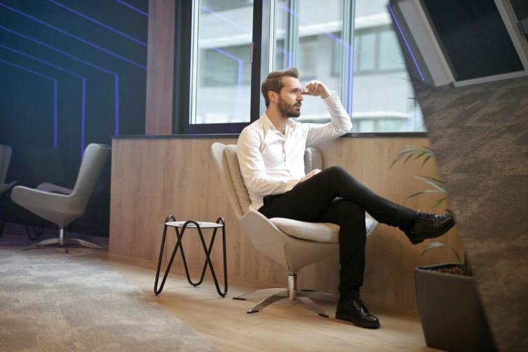A thoughtful man in a modern office interior, sitting and looking outside.