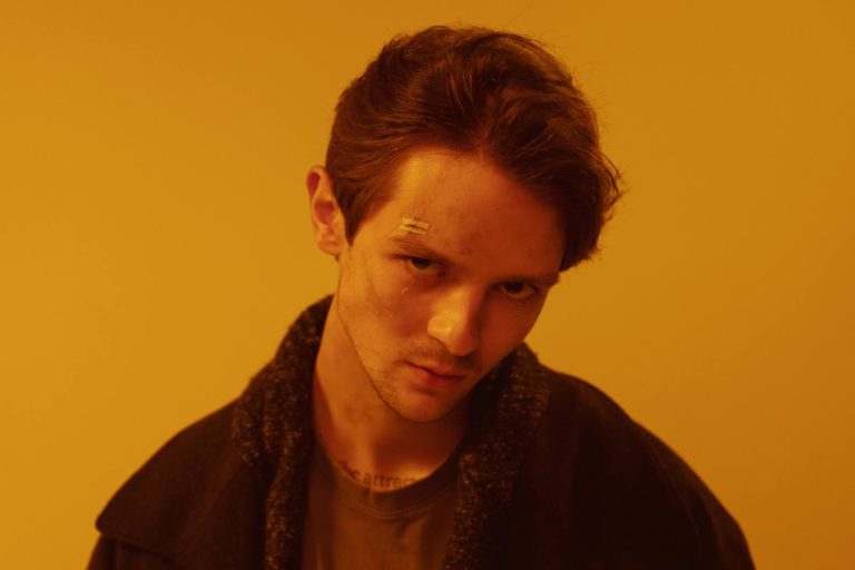 Close-up of a man with a cyberpunk aesthetic against a warm orange background.