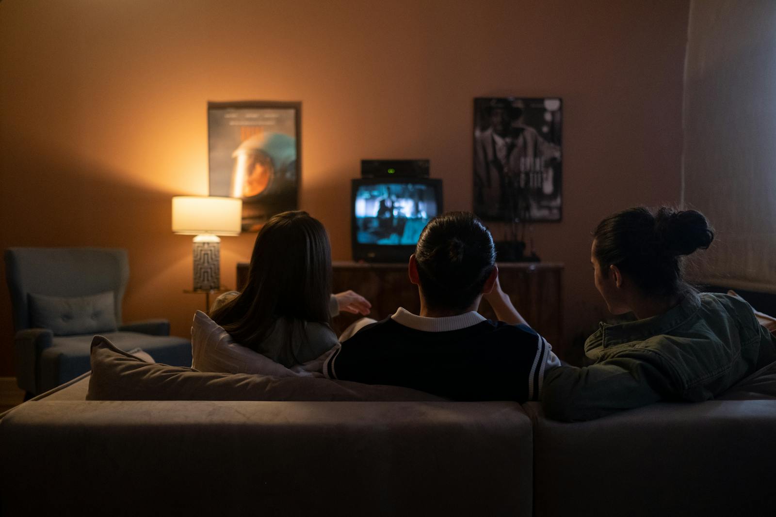 Three people enjoying a relaxed movie night at home, sitting on a couch in a cozy living room.