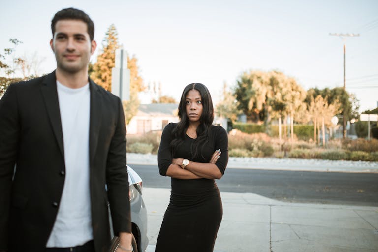 A couple facing relationship tension outdoors with arms folded, expressing emotions.