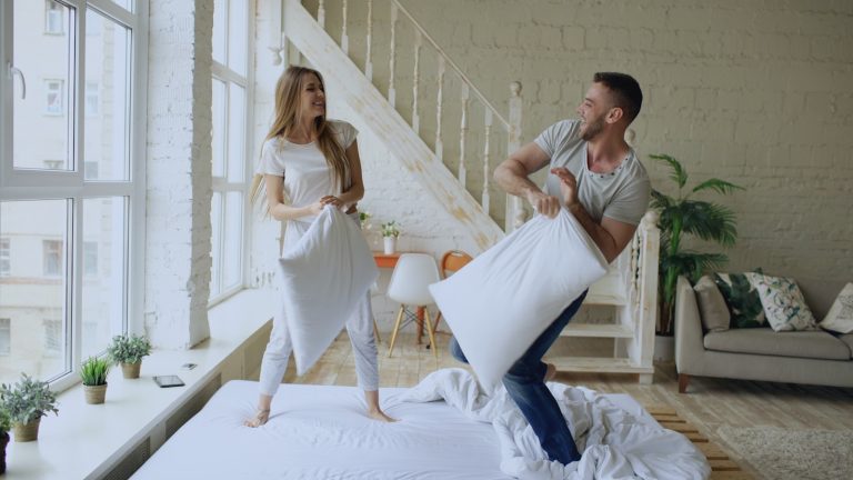 Couple having a playful pillow fight on a bed.