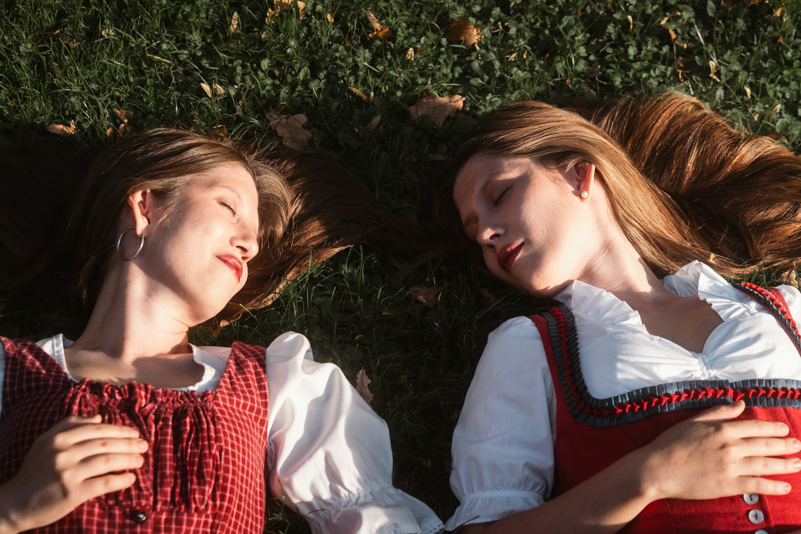 Two young women in traditional bavarian dress lying on grass.
