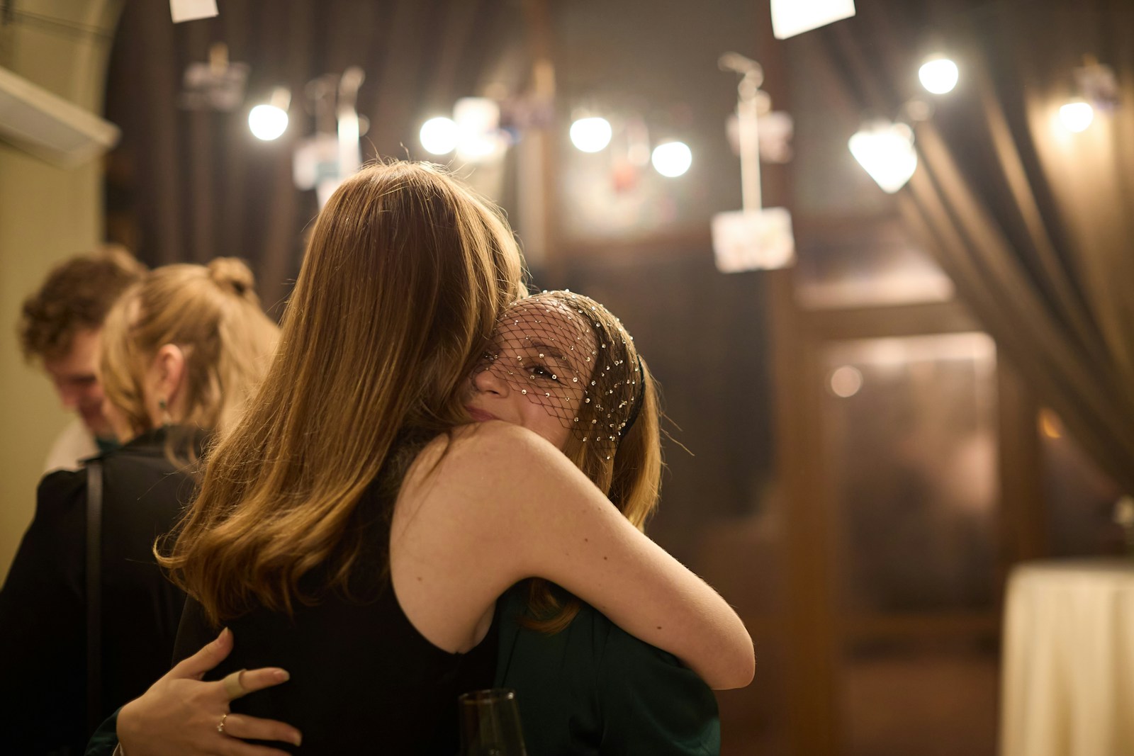 Two women embracing warmly indoors with string lights above