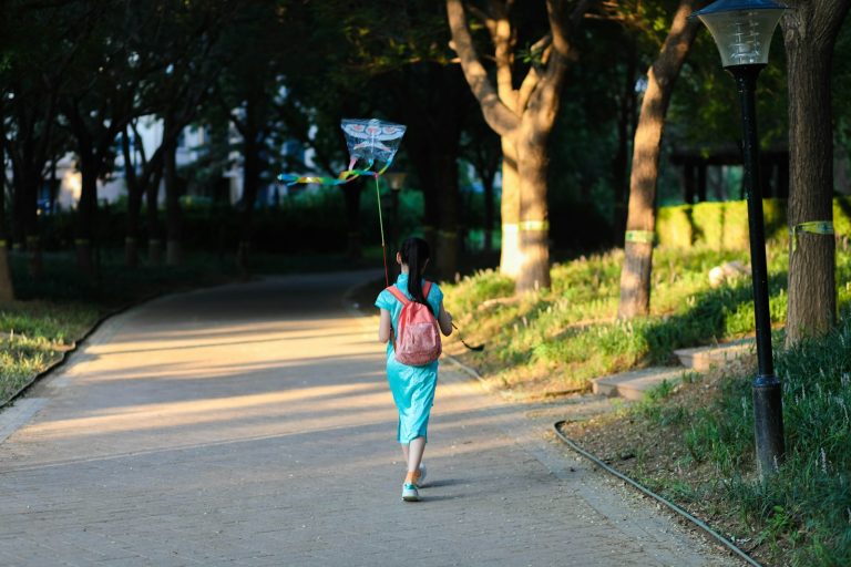 a woman walking down a sidewalk holding a kite