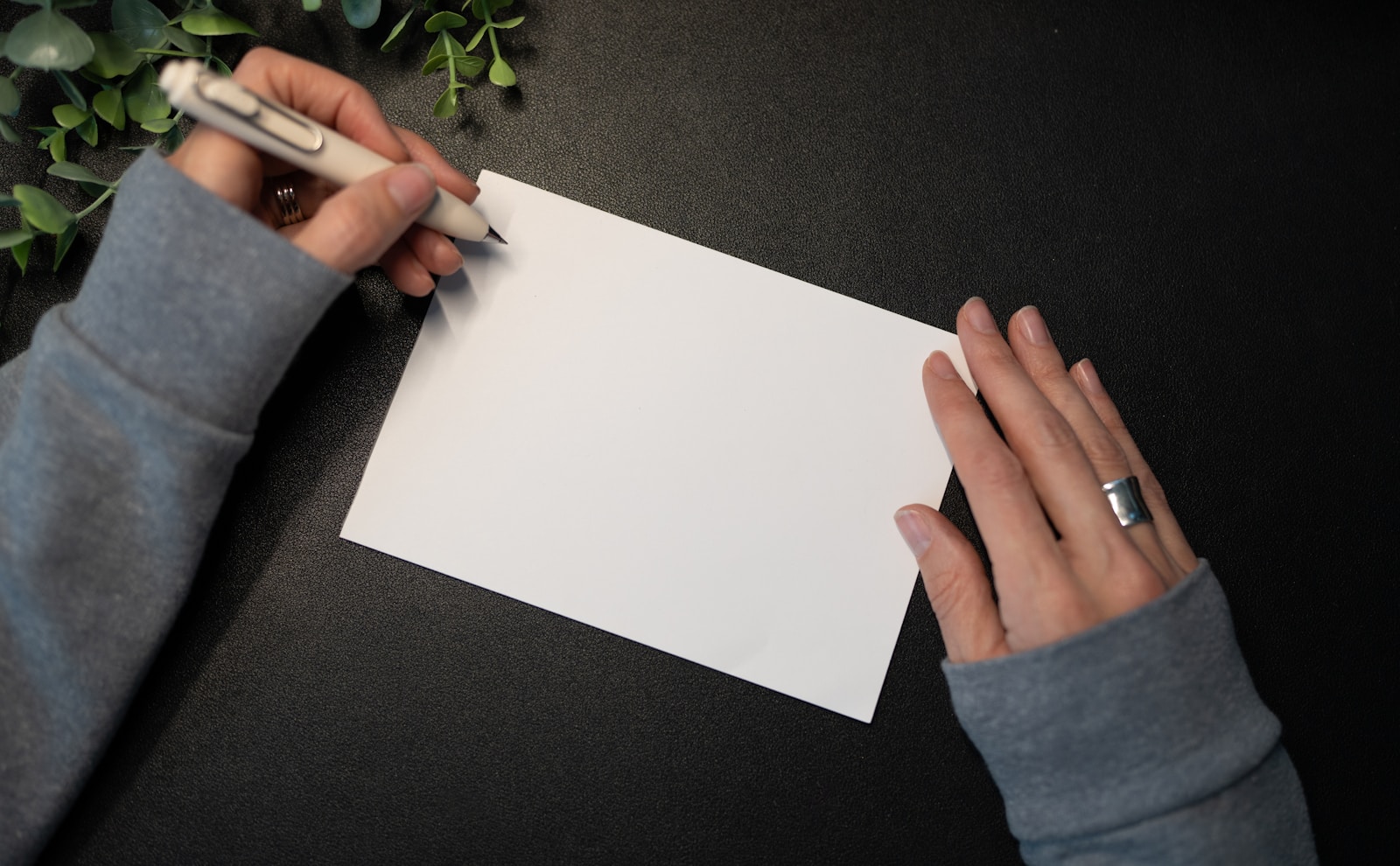 Hands writing on a blank card with greenery.