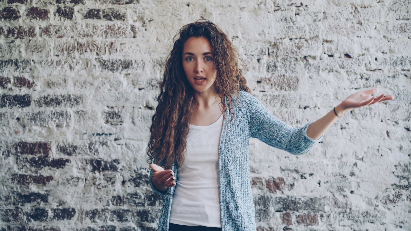 Woman gesturing while speaking against brick wall.