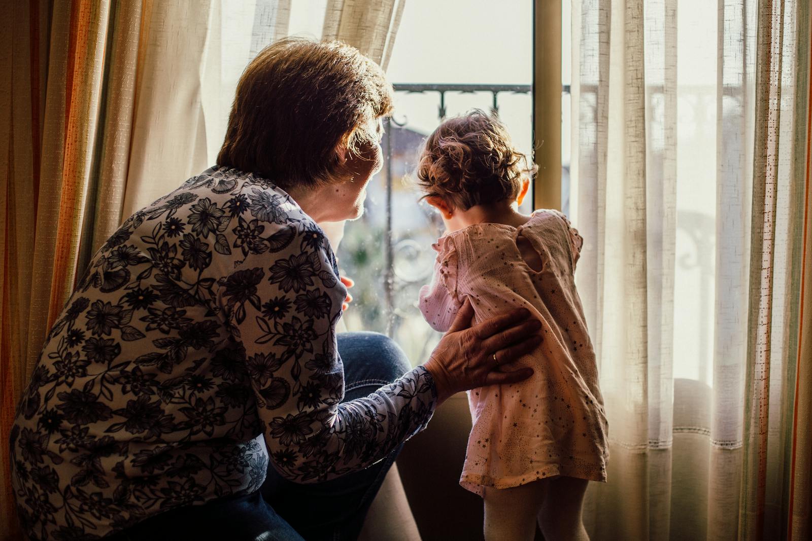 A loving moment between grandmother and grandchild near a window filled with sunlight.