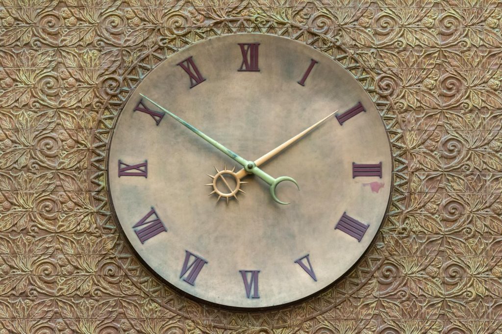 A vintage-style wall clock set against a textured, ornate background with Roman numerals.