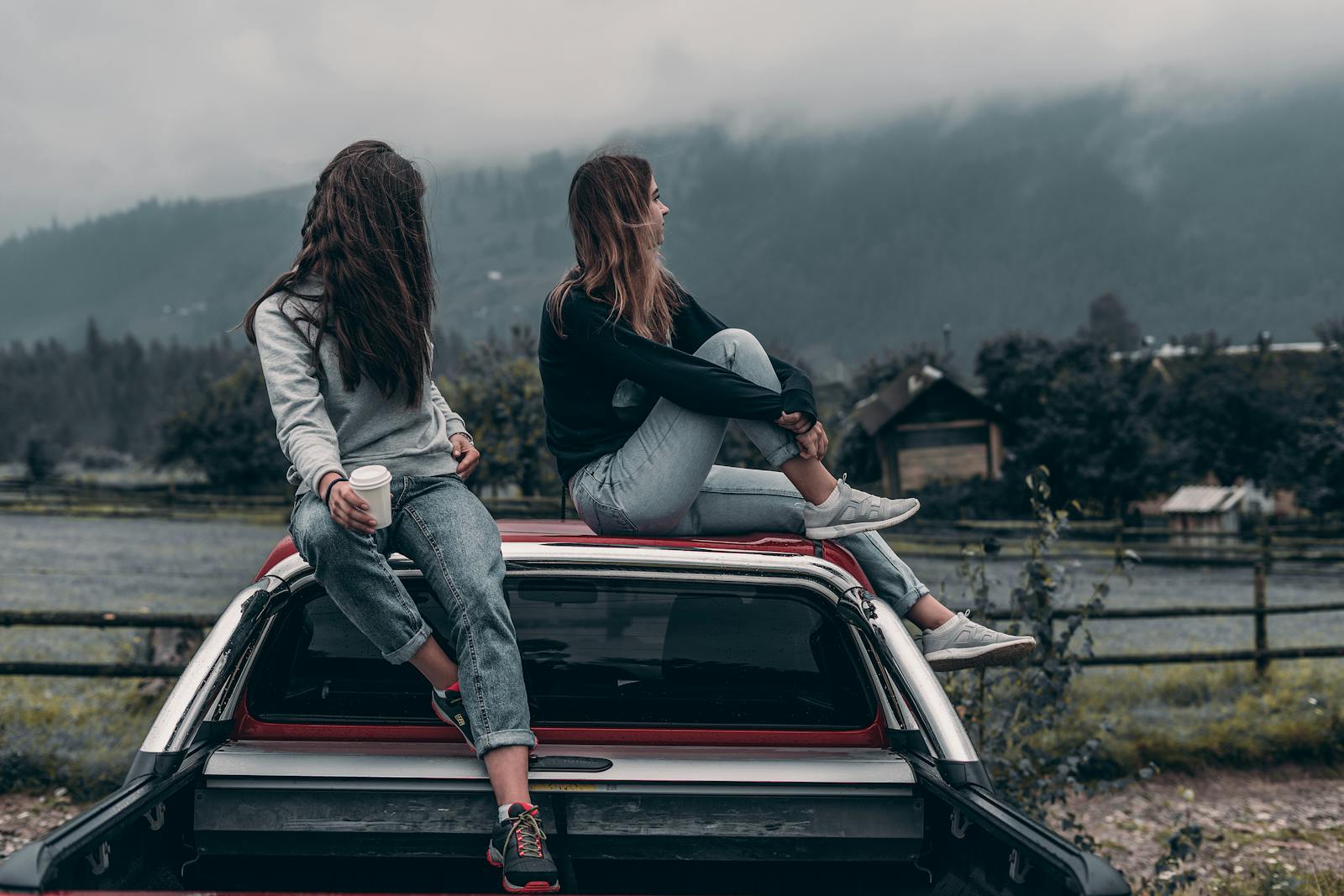 Two young women sitting on a car, enjoying the serene mountain landscape in Romania.