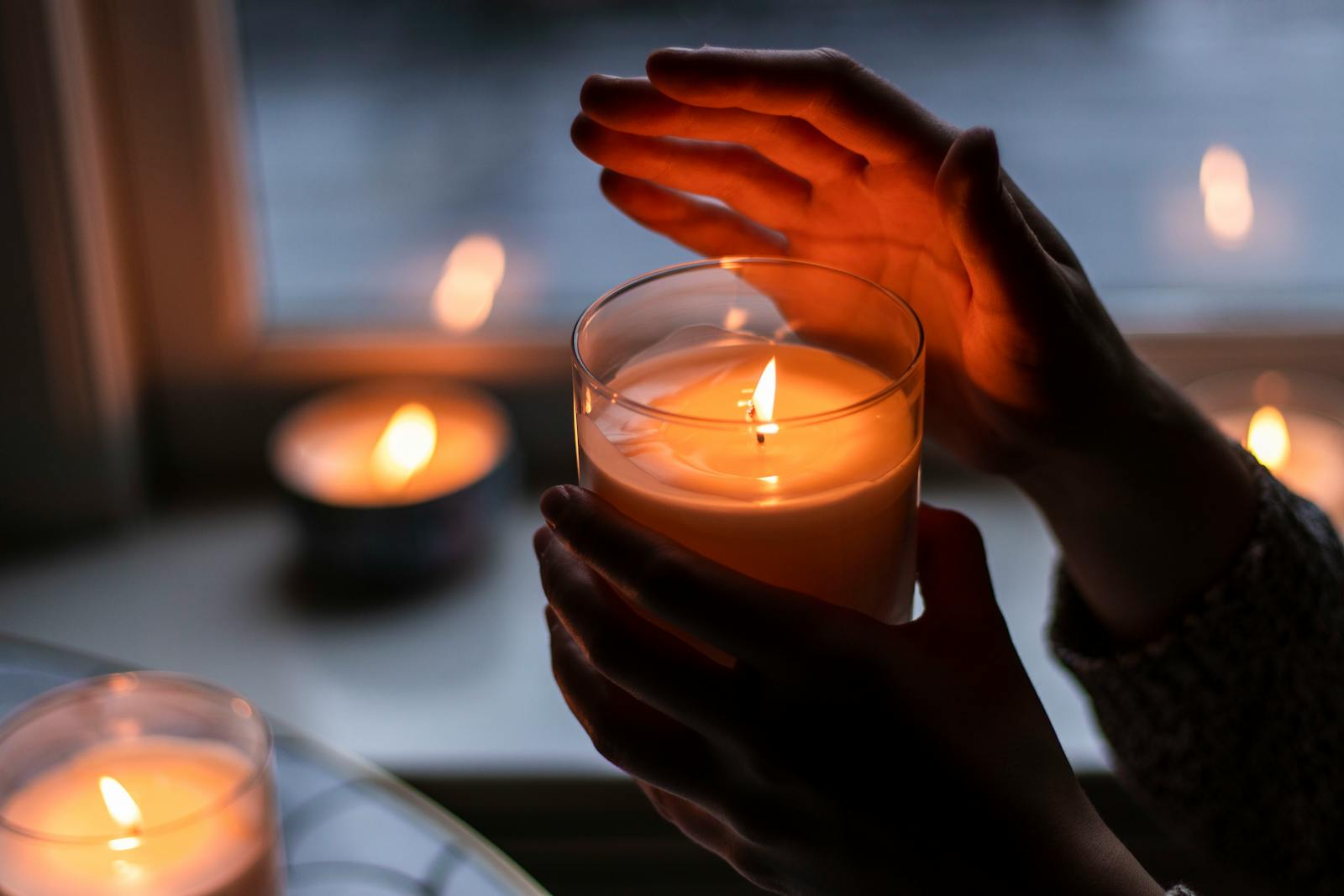 Warm candlelit ambiance with hands gently holding a burning candle indoors.