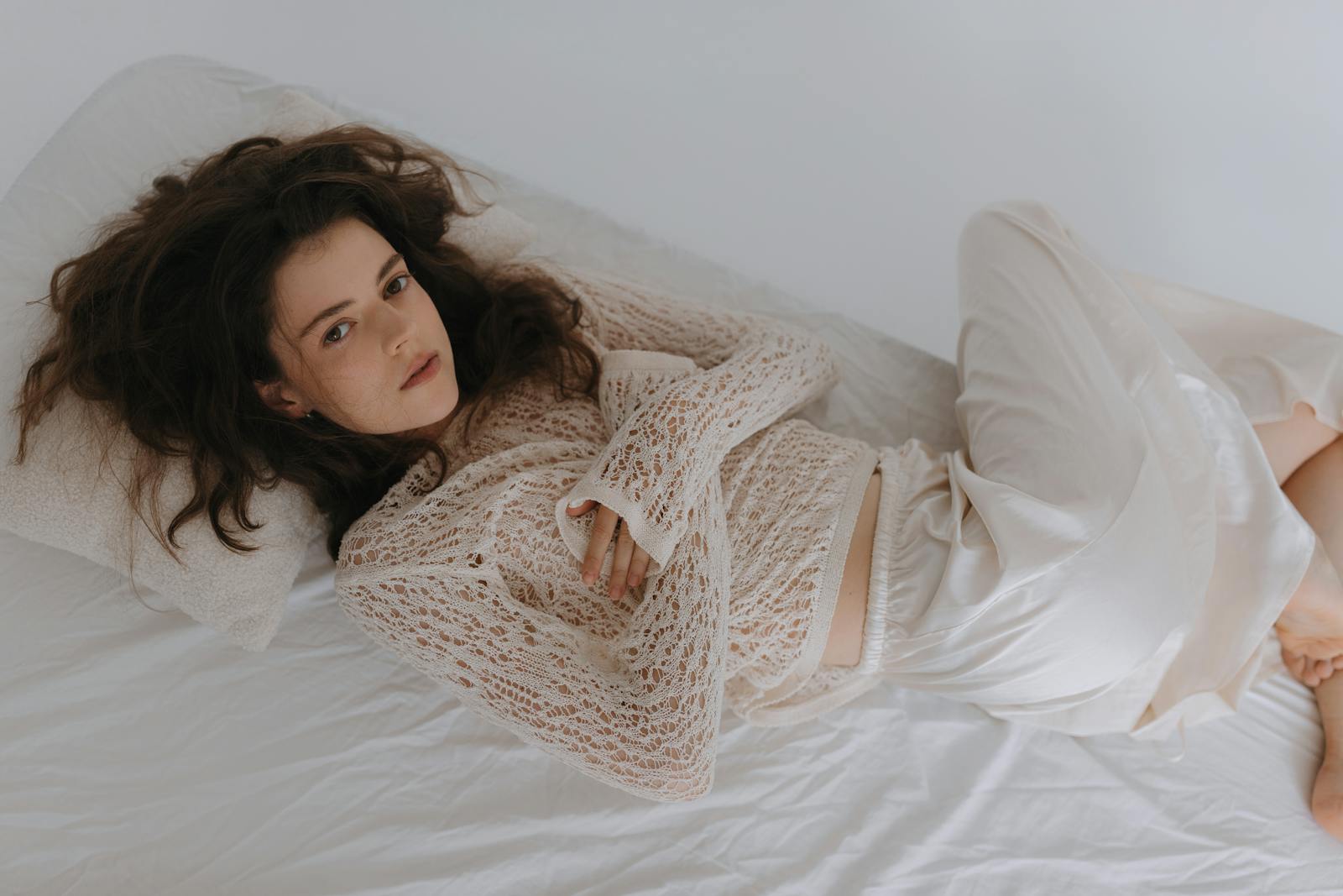 Woman in white lace clothing lying on a bed, exuding calm and elegance.