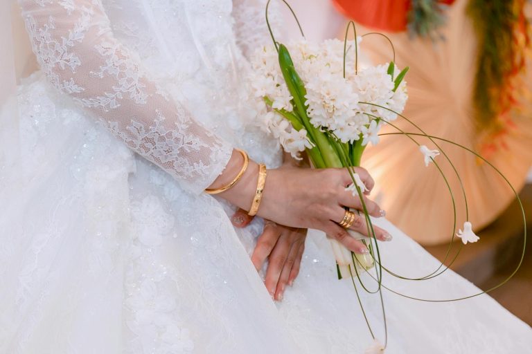 Close-up of a bride in lace dress holding a white floral bouquet. Elegant and romantic wedding theme.