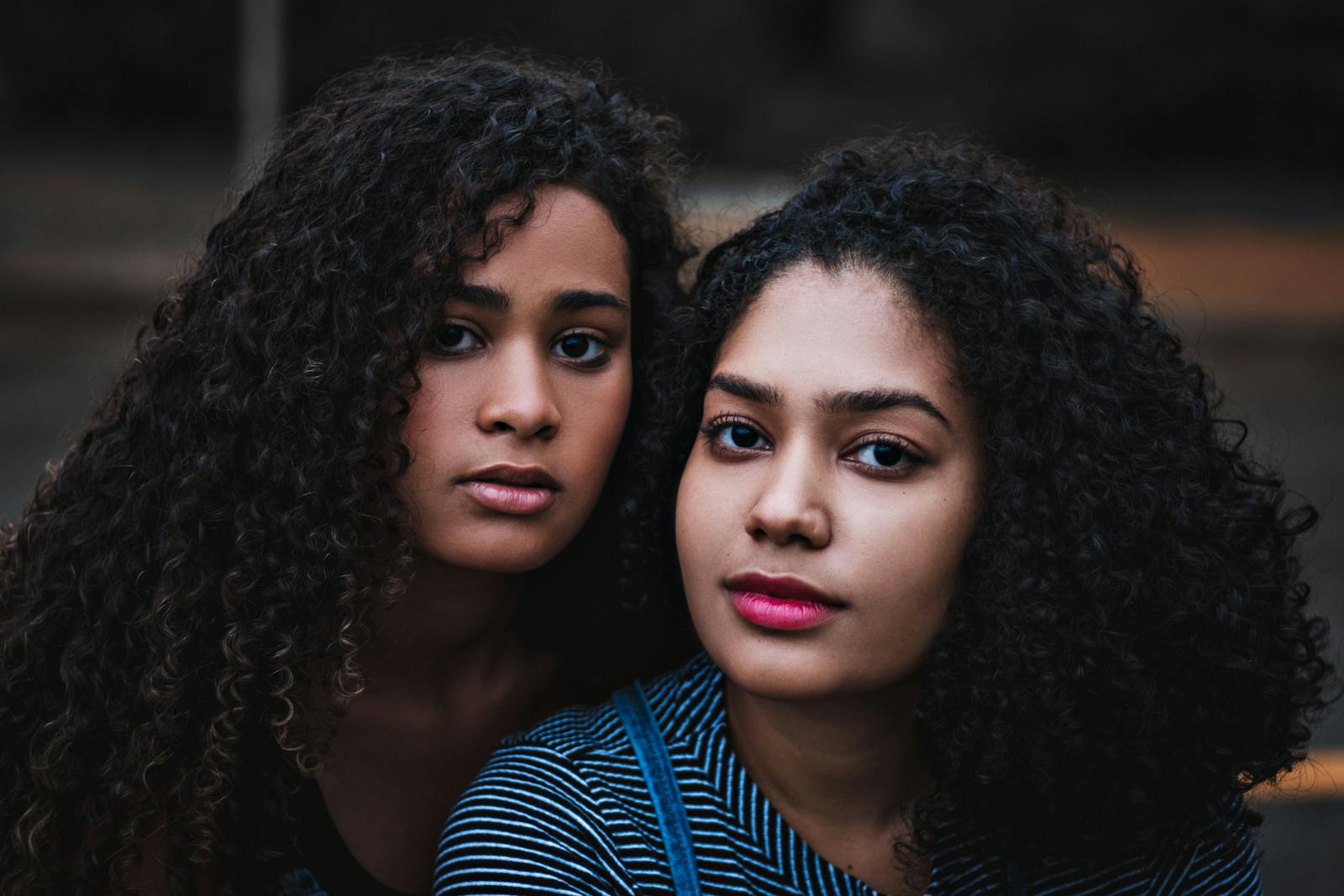 Close-up portrait of two women with curly hair in a serene outdoor setting.