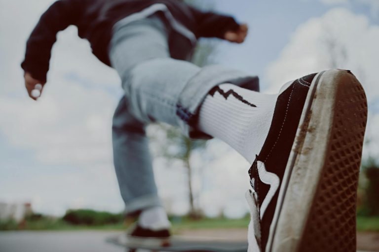 Low-angle view of a skateboarder in motion wearing sneakers and white socks on a bright day.