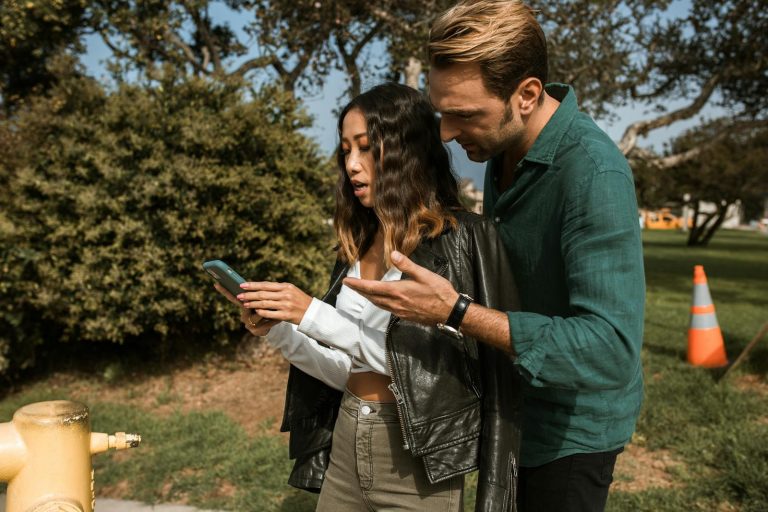 A couple having a disagreement outdoors, focusing on a cellphone. Emotions are visible.