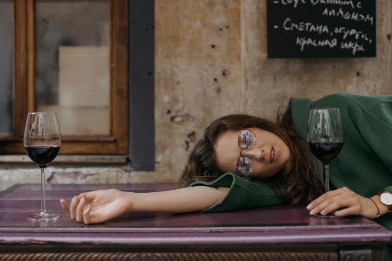 Young woman in green coat relaxing with wine at café table, capturing a serene moment.
