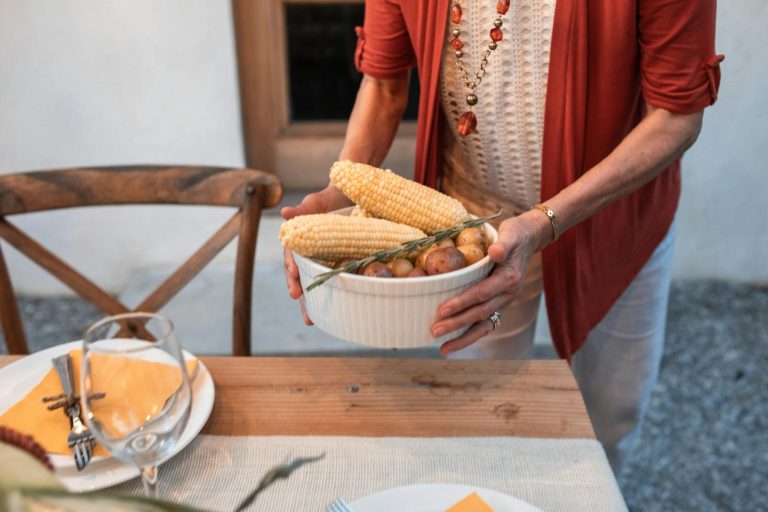 A woman sets a dinner table with corn and potatoes for a fall gathering.